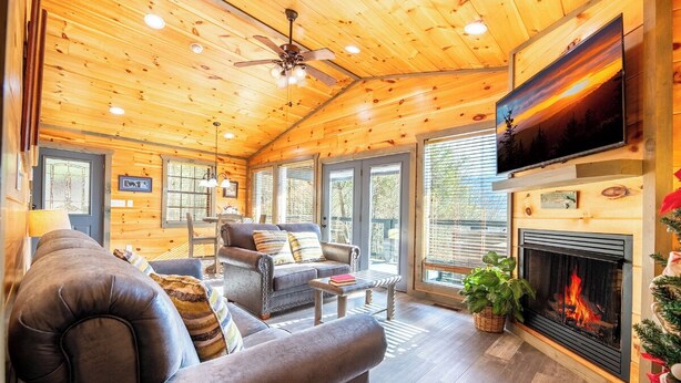 A cozy cabin interior with a fireplace, leather sofas, and a television. - Cozy Mountain Cabin w/ VIEWS | Hot Tub + Fireplace (Cosby)