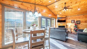 A wooden cabin interior with a dining area, sofa, and fireplace. - Cozy Mountain Cabin w/ VIEWS | Hot Tub + Fireplace (Cosby)