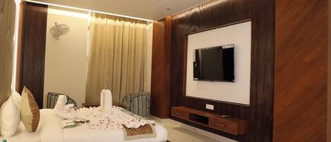 A modern bedroom with a large bed, a flat-screen TV mounted on the wall, and a wooden panel design.