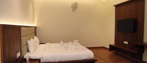 A bedroom with a bed, bedside table, TV, and a wall-mounted fan.