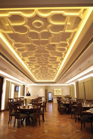Ein Speisesaal eines Hotels mit Holztischen und -stühlen, einem modernen Deckenstil und einer Rezeption.