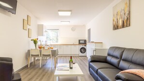 Een moderne woonkamer met een zwarte leren bank, een witte salontafel, en een eethoek met een tafel en stoelen.