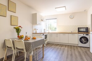 Eine moderne Küche mit weißen Schränken, einem eingebauten Backofen, einer Mikrowelle und einer Waschmaschine. Ein Esstisch mit Stühlen und eine Blumenvase ergänzen das Bild.