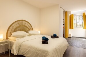 A hotel room with a bed, a nightstand, a wicker headboard, and a window with yellow curtains.