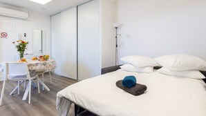 Een hotelkamer met een bed, een bureau met stoel, een spiegel, een nachtkastje en een wandlamp.