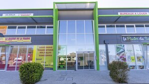 Een bedrijfsgebouw met een groene gevel, grote ramen en reclame voor diverse bedrijven, waaronder een bakkerij en een bakkerij genaamd 'La Maison de la Violette'.