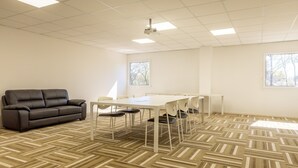 Een vergaderruimte met een witte tafel, stoelen, een zwarte bank en een kamerbreed tapijt met dessin.