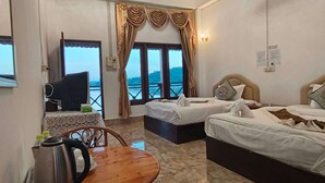 A hotel room with two beds, a wooden table, a TV, and a view of the sea. - Houayxai Riverside Phonevichith Hotel (Houayxay)