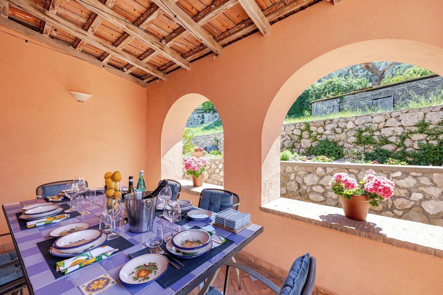Un coin repas avec une table dressée pour quatre personnes, un mur en pierre et une vue sur la verdure.