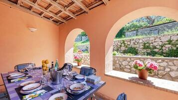 Un coin repas avec une table dressée pour quatre personnes, un mur en pierre et une vue sur la verdure.