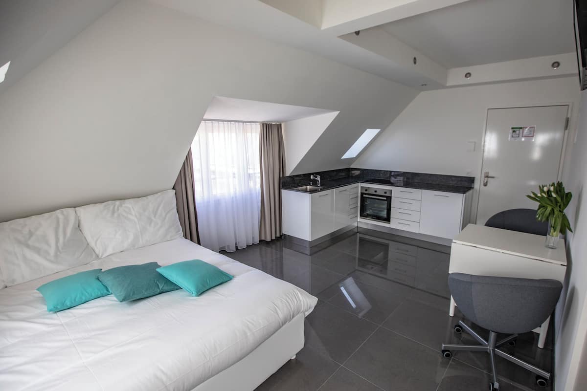 A modern hotel room with a large bed, a desk, and a kitchenette.