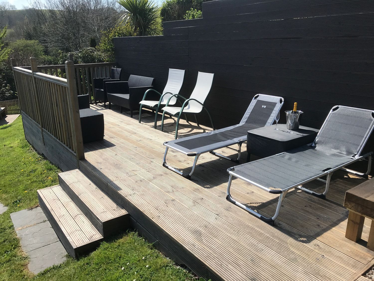 Una terraza con sillas de descanso y una mesa, rodeada por una cerca de madera y follaje.