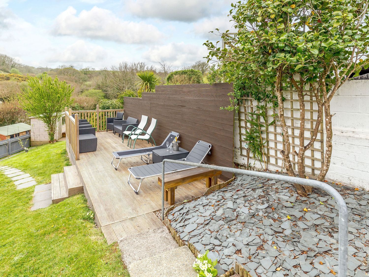 Un patio con mobiliario exterior, una terraza de madera y un camino de piedra.