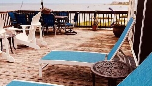 Een houten terras met ligstoelen en een rode parasol, met uitzicht op een wateroppervlak.