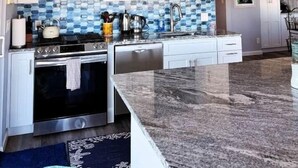 Een moderne keuken met witte kasten, een roestvrijstalen fornuis, een magnetron en een betegelde spatwand.