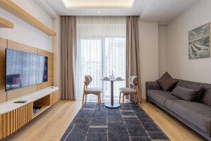 A modern living room with a flat-screen TV, a grey sofa, two chairs, a small round table, and a large window with sheer curtains. - New Flat near Cevahir Mall, Şişli (İstanbul)