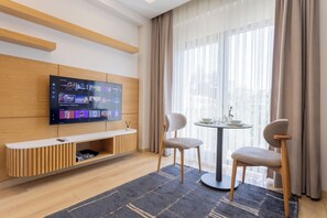 A modern living room with a flat-screen TV, a wooden bench, two chairs, a round table, and a large window with curtains. - New Flat near Cevahir Mall, Şişli (İstanbul)