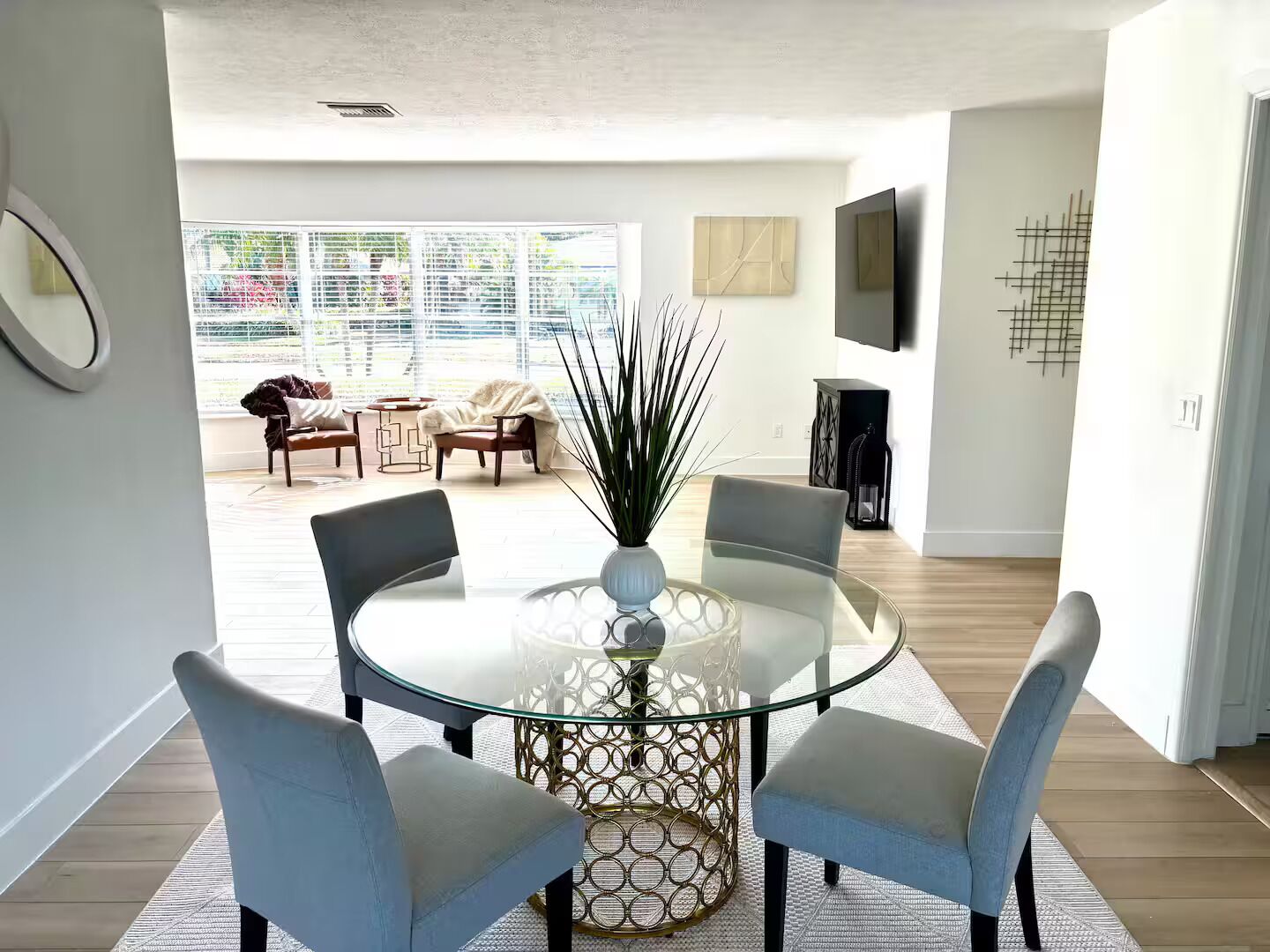 A modern dining area with a glass table, four chairs, and a decorative vase.