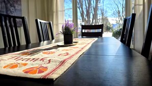 A dining area with a table set for two, a potted plant, and a view of trees through the window.