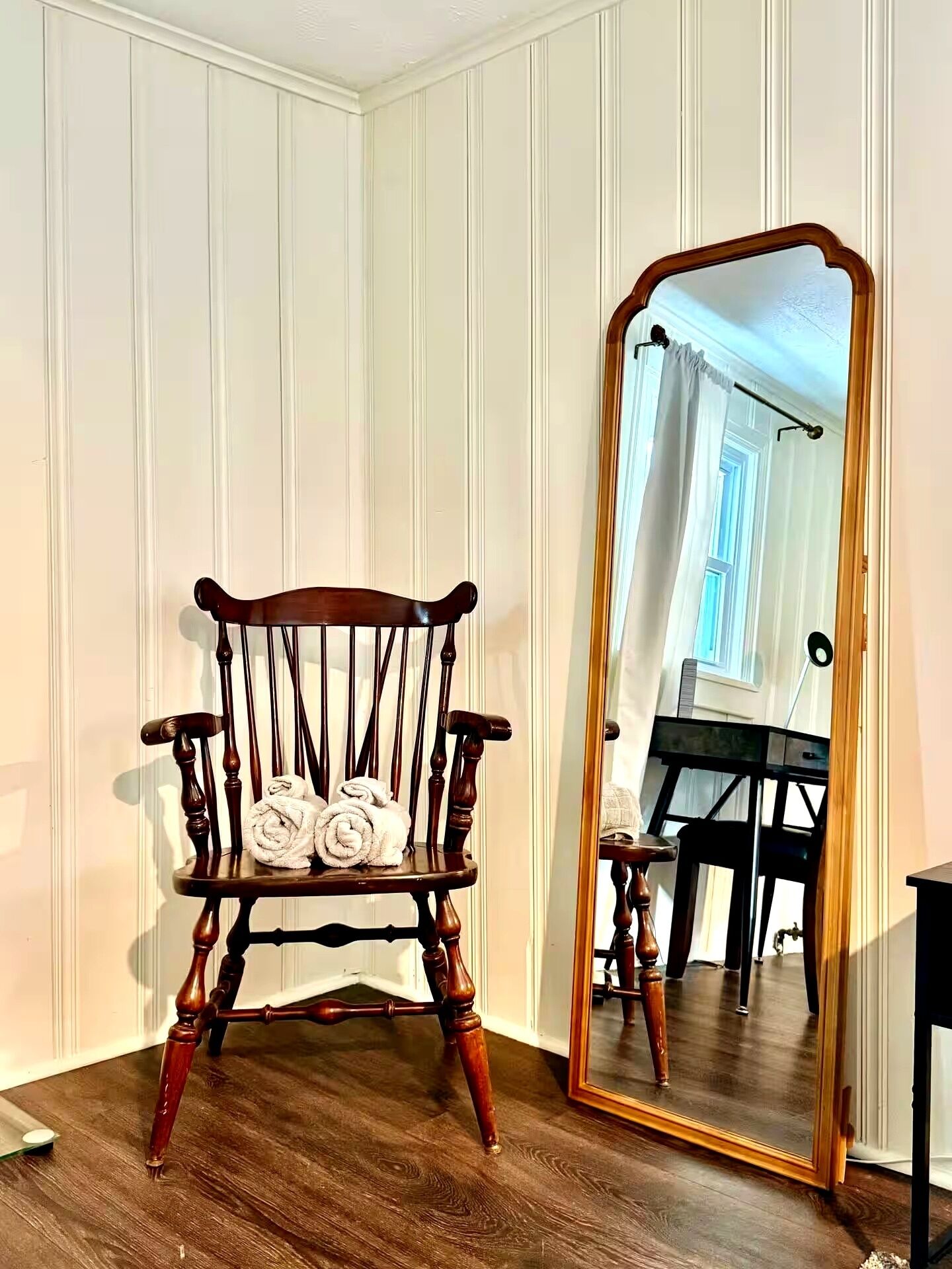A wooden chair with rolled towels placed on it, positioned in front of a mirror with a wooden frame.