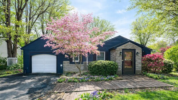 A residential house with a garage, a front porch, and a well-maintained garden with flowering plants.