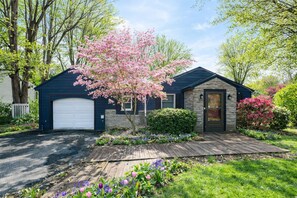 A residential house with a garage, a front porch, and a well-maintained garden with flowering plants. - Spacious 4-Bed 2-Bath Ranch in Rochester, Game Room, RIT, Genesee River, Airport (Rochester)