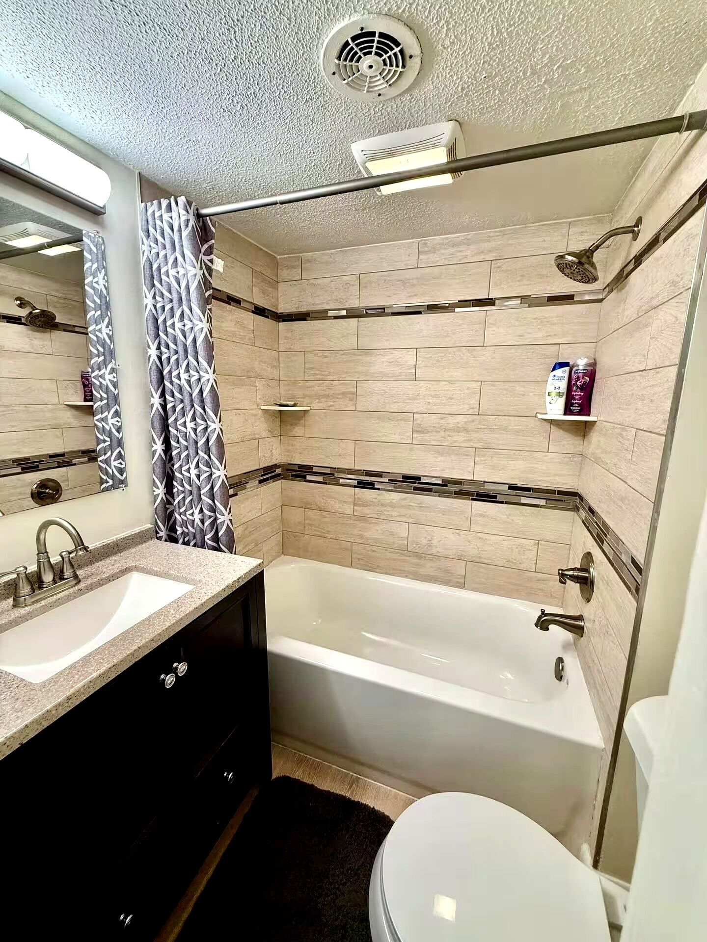 Een badkamer met een bad, wastafel en toilet. Er staan planken met toiletartikelen en een douchekop boven het bad.
