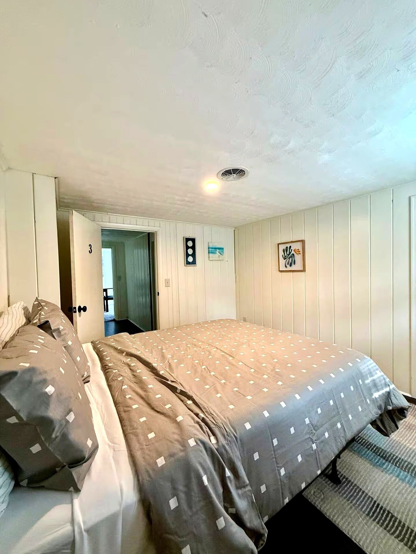 A bedroom with a bed, a door, a wall-mounted light, and a small picture.