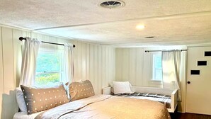 A bedroom with a large bed, two bedside tables, a window with curtains, and a door with a small window.