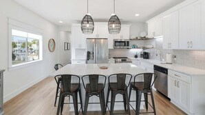 A modern kitchen with white cabinets, stainless steel appliances, and a central island with bar stools. - Seagrove Crush- Renovated- Steps to Private Beach! (Santa Rosa Beach)
