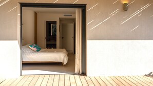 A room with a bed, a wooden floor, a wall-mounted light, and a door leading to another room. - Contemporary sea-view villa with large infinity pool and walking distance to the beach (Zonza)