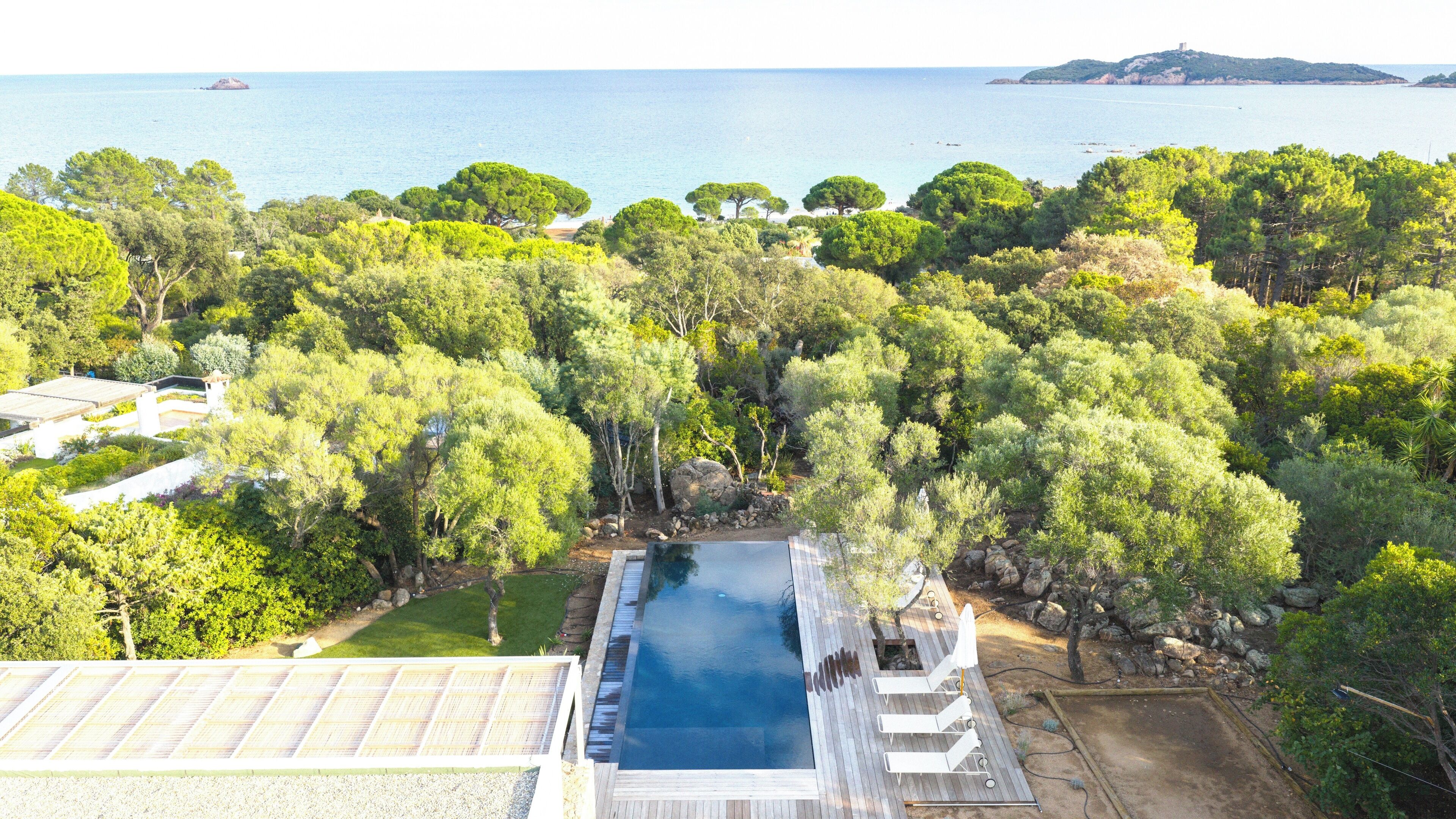 Vista aerea di una proprietà con piscina circondata da vegetazione lussureggiante e vista sul mare.