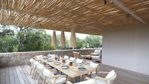 A wooden deck with a table set for dining, surrounded by wicker chairs, under a bamboo canopy. - Contemporary sea-view villa with large infinity pool and walking distance to the beach (Zonza)