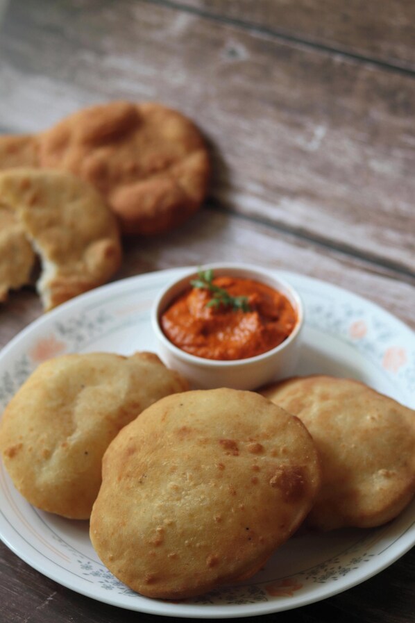 A plate with three round, golden-brown fried items and a small bowl of red sauce. - HOTEL SR PALACE NEAR IGI DELHI AIPRORT (New Delhi)