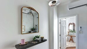 Um corredor com uma prateleira preta com objetos decorativos, um espelho grande com moldura ornamentada e uma porta que dá para outro quarto.