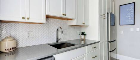 A modern kitchen with white cabinetry, a herringbone tile backsplash, a stainless steel refrigerator, and a dishwasher.