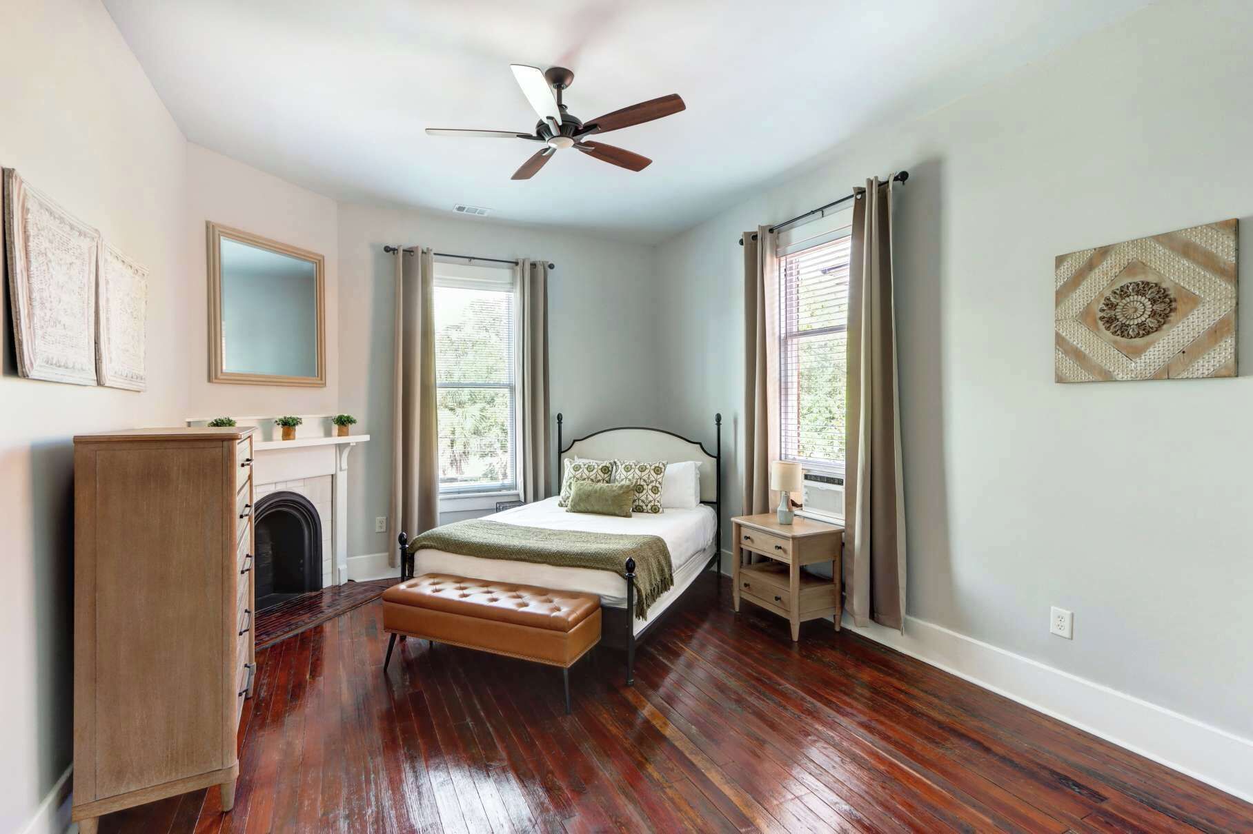 A bedroom with a bed, a wooden bench, a dresser, a ceiling fan, and a window with curtains.