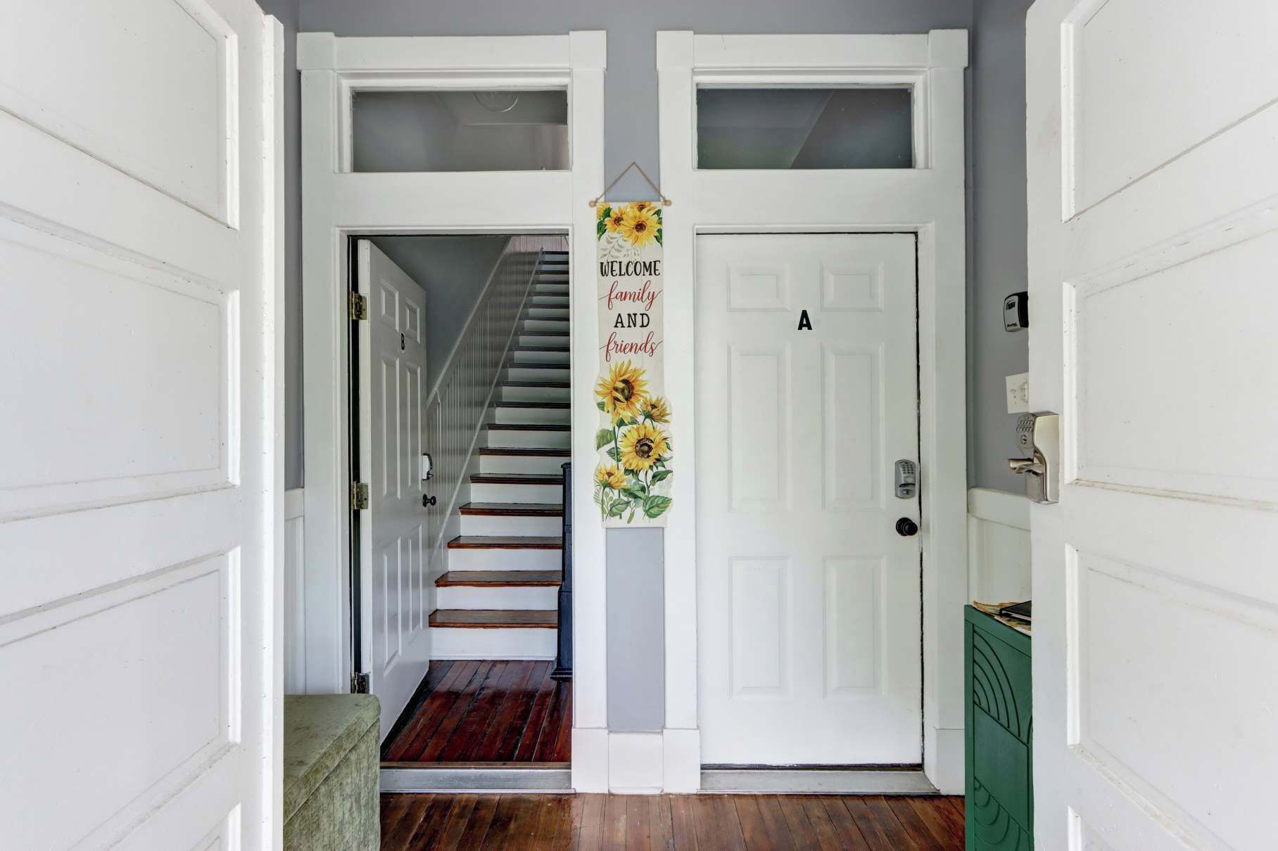 Un pasillo con una escalera de madera, puertas blancas y un cartel que dice 'WELCOME family and friends'.