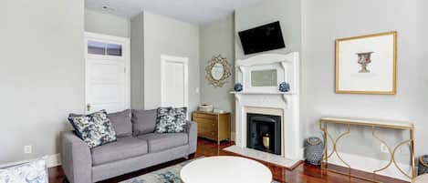 A living room with a gray sofa, a round white coffee table, a fireplace, and a television mounted on the wall.