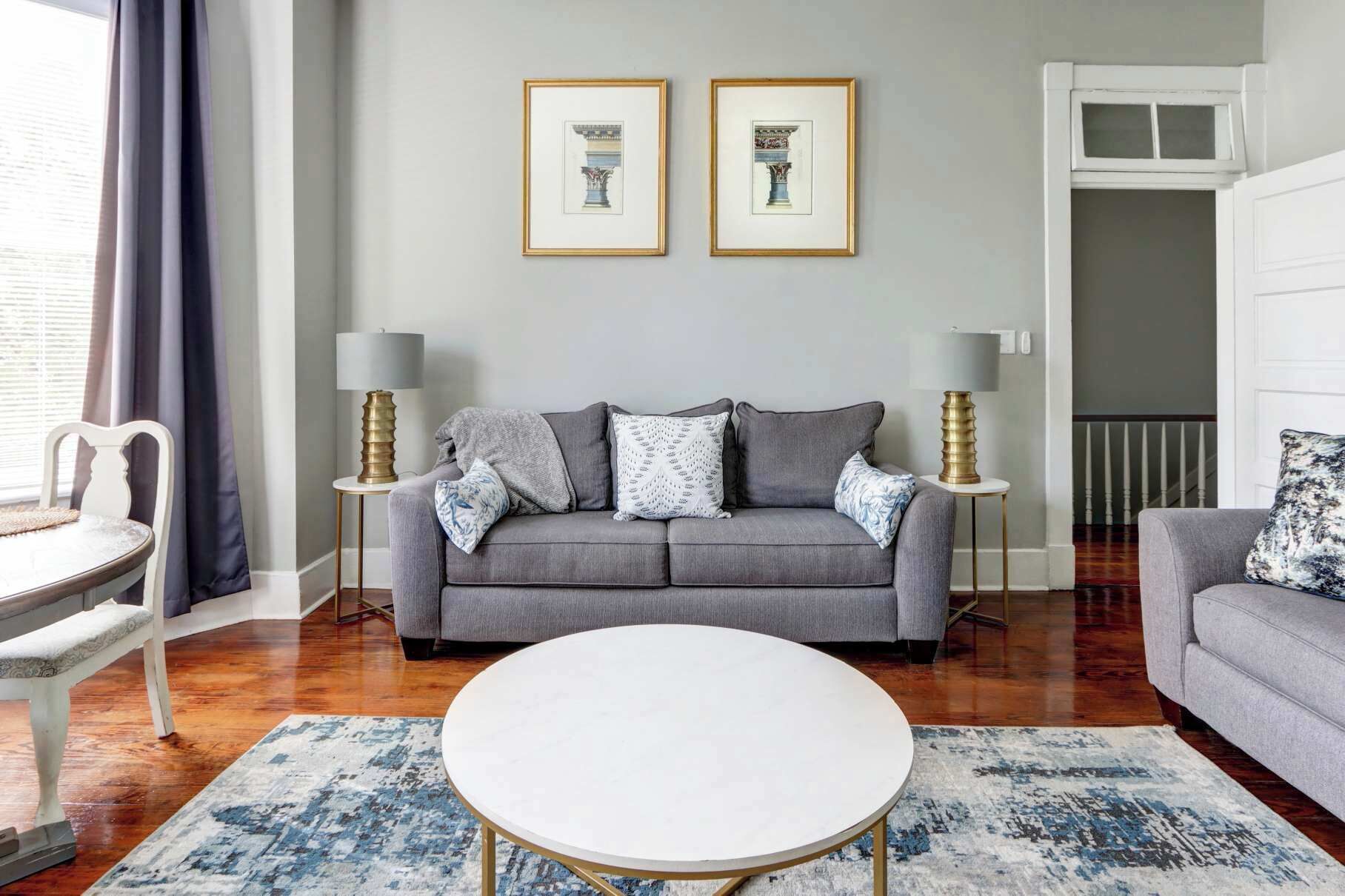 Un salon avec un canapé gris, deux tableaux encadrés, une table basse blanche et un tapis bleu à motifs.