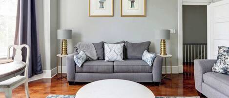 Un salon avec un canapé gris, deux tableaux encadrés, une table basse blanche et un tapis bleu à motifs.