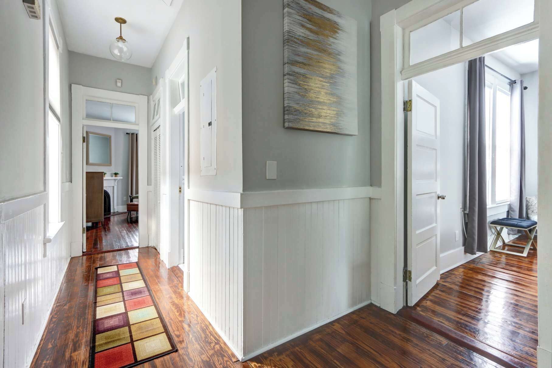 A hallway with wooden flooring, white wainscoting, and a large abstract painting on the wall.