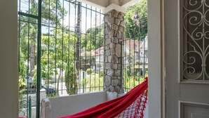A balcony with a red fabric, stone pillar, and metal railing. - Casa p 8 Pessoas c Varanda a 400m Museu Imperial (Petrópolis)