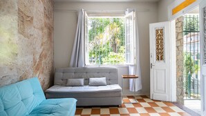 A room with a grey sofa, a blue armchair, a window with curtains, a door with a decorative panel, and a checkered floor. - Casa p 8 Pessoas c Varanda a 400m Museu Imperial (Petrópolis)