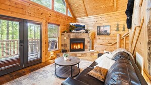 A wooden cabin interior with a fireplace, a leather sofa, and a dining table. - Little Woods Cabin | Family-Friendly w/ Games! (Sevierville)