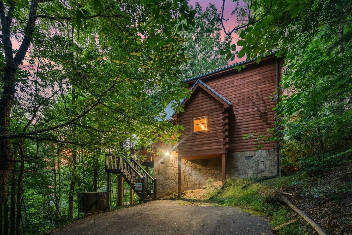A log cabin with a stone foundation, a wooden staircase, and a view of the surrounding forest.