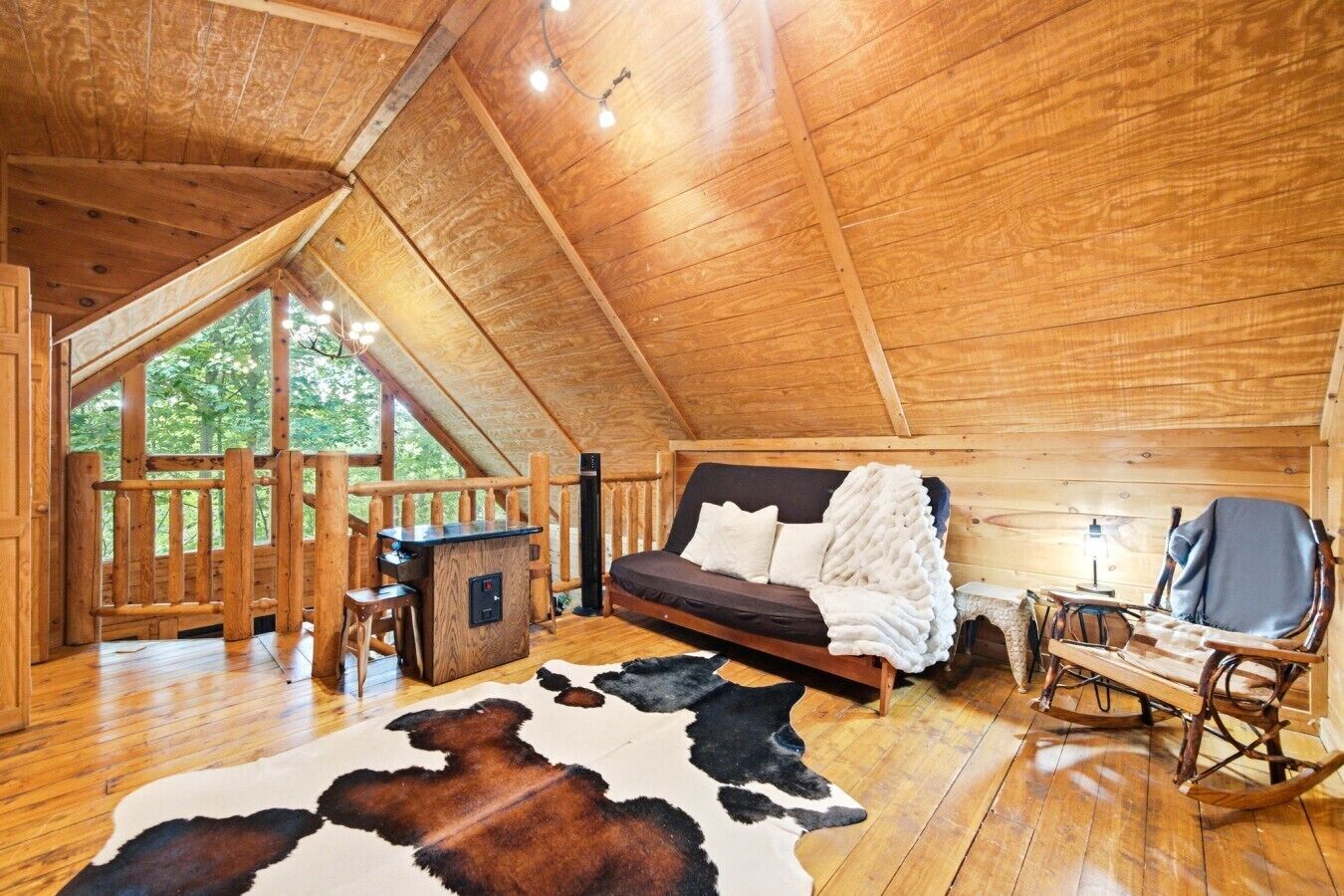 A wooden cabin with a loft bedroom, a wooden desk, and a rocking chair.
