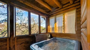 Eine Holzhütte mit Whirlpool, großen Fenstern und Blick auf Bäume.
