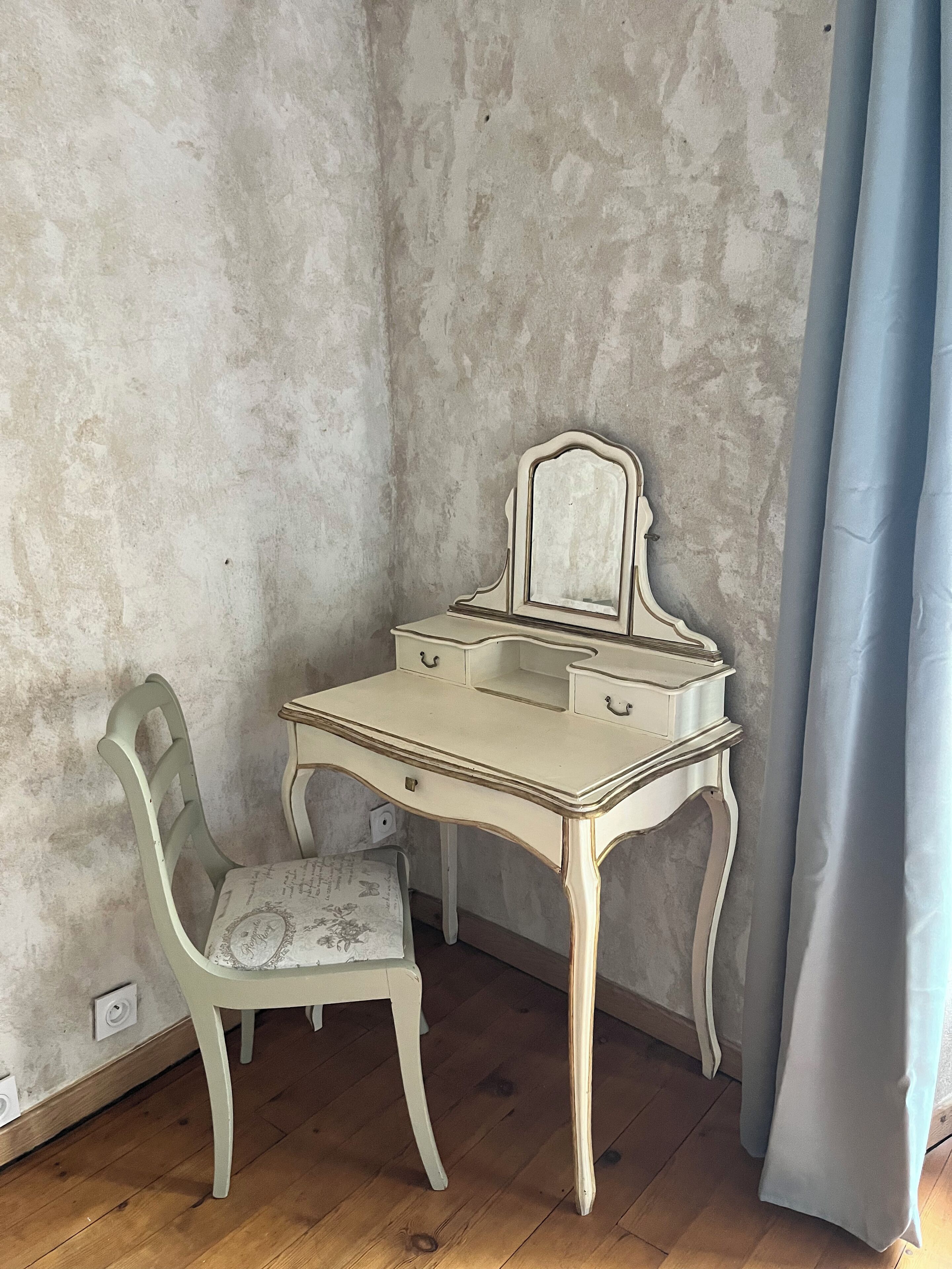 A corner room with a white desk and chair, a blue curtain, and a textured wall.
