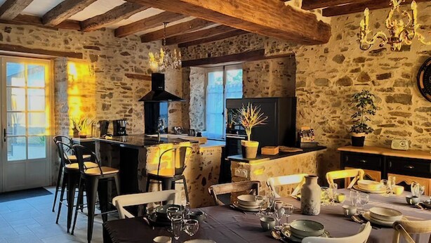 A rustic kitchen with stone walls, wooden beams, a chandelier, and a dining area set for a meal. - La Pierre du Bonheur" village house for 2 to 8 people (Saint-Denis-d'Anjou)